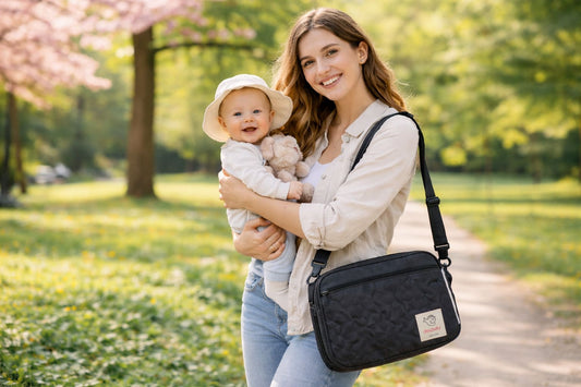 Maman portant un sac à langer en bandoulière avec bébé dans les bras se promène dans un parc au printemps