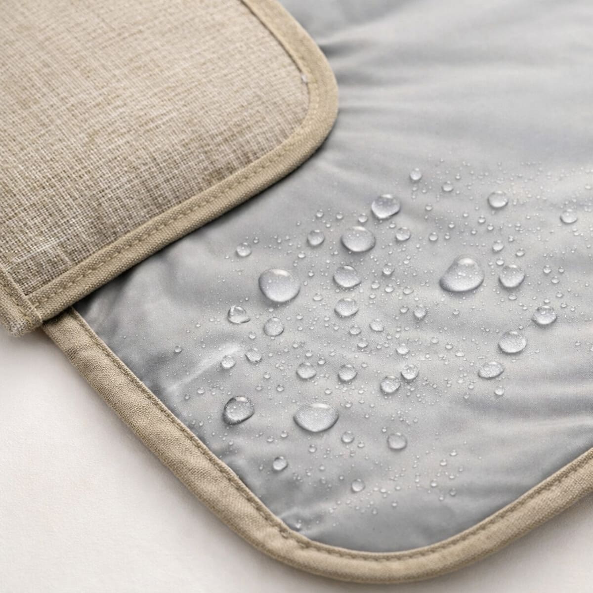 Tapis à langer nomade Nomade+  imperméable avec gouttes d’eau sur surface grise et tissu beige détaillé 