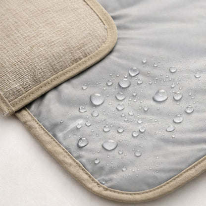 Tapis à langer nomade Nomade+  imperméable avec gouttes d’eau sur surface grise et tissu beige détaillé 