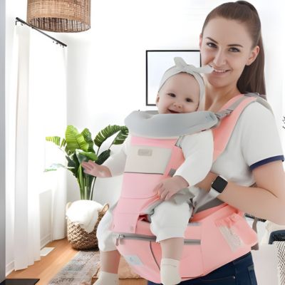 maman portant bébé face au monde dans le salon avec porte-bébé ergonomique Aventurier en Herbe rose